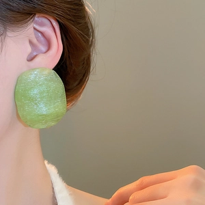 Close-up of a model wearing large green round earrings with a textured resin finish