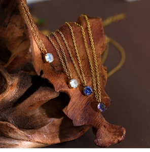 Detail view of four-prong round zircon pendants on gold chains over dark wood background