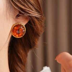 Close-up of vintage gold rimmed amber resin earrings on model for a retro aesthetic