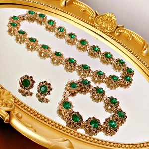 Dettaglio di un set di gioielli vintage a fiore dorato con cristalli verdi su specchio