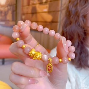 Close-up of sunstone beads with golden Pi Xiu charm and Fortune pendant on a wrist