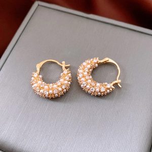 Macro shot of 18k gold plated pearl and zircon hoop earrings on a grey jewelry box