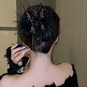 Detail view of a black feather butterfly hair claw with metallic tassels on a model hair