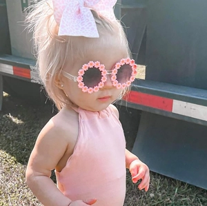 Pink flower-shaped kids sunglasses with matching bow headband on a young girl model