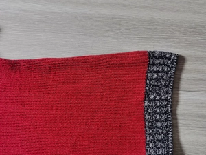 Dettaglio maglione rosso con bordo a contrasto in maglia maculata bianca e nera