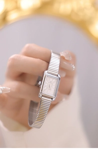 Close-up of a silver rectangular quartz watch with a metal stretch band on a wrist