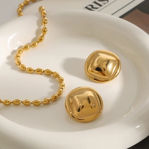 Detailed close-up of a gold square stud earring and oval bead necklace set on ceramic