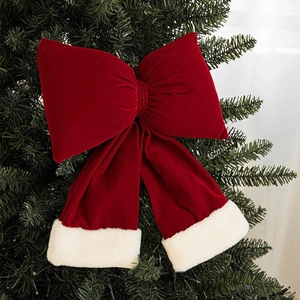 Large red velvet Christmas bow with white plush trim hanging on a green Xmas tree