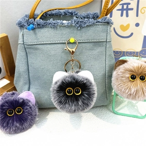 Close-up of fuzzy plush cat ball keychains with gold metal rings on a denim bag