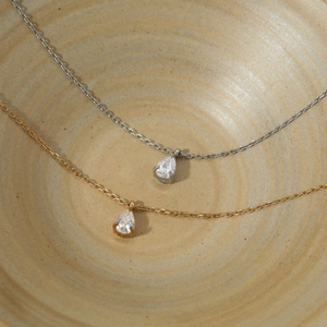 Elegant gold and silver teardrop crystal pendant necklaces in a minimalist ceramic bowl