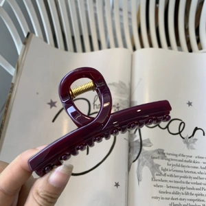 Gros plan sur la pince à cheveux bordeaux élégante avec ressort doré sur un magazine