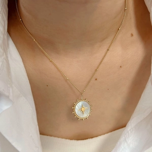 Gold starburst pendant necklace with white shell inlay worn by a female model