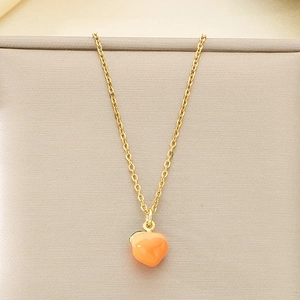 Detail of a golden necklace featuring a sweet orange enamel peach pendant on beige fabric