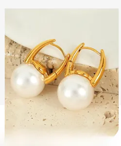 Detailed close-up of gold pearl drop earrings on a textured stone pedestal