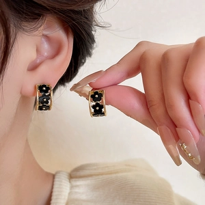 Detail of C-shaped floral earrings with black petals and gold edges on model