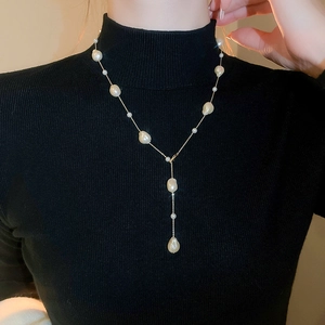 Y-shaped gold beaded necklace with baroque pearls styled over a black sweater dress