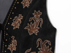Détail de broderies florales brunes et perles dorées sur un gilet en velours noir