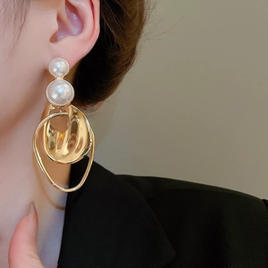 Close-up of a model wearing gold geometric earrings with pearls and irregular circles