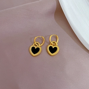 Close-up of golden heart earrings with black enamel inlay and sunburst texture
