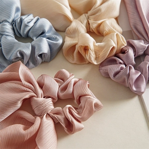 Detail showing various colors of smooth satin ponytail scrunchies with pleated texture