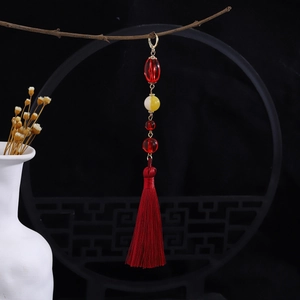 Detailed view of red tassel pendant with pearls hanging on a wooden branch