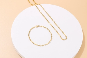 Close-up of a minimalist gold link chain necklace and bracelet set on a white stand
