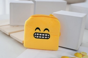 Detail of yellow plush coin purse with embroidered smile emoji and yellow zipper