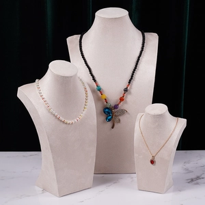 Three elegant necklaces on beige velvet busts featuring pearls, butterfly, and ruby pendants