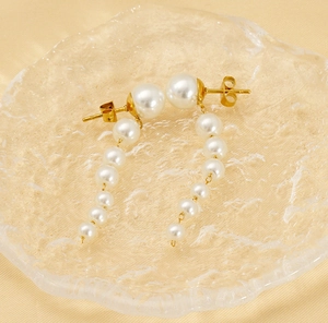 Detail of long pearl tassel earrings with gold-tone studs resting on silk fabric