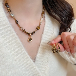Macro detail of tiger eye beaded necklace and twisted gold ring worn by a model