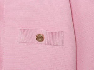 Dettaglio del cardigan rosa in maglia con trama fine e bottone dorato sulla tasca