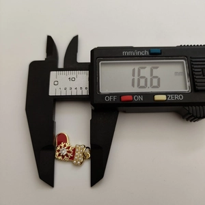 Macro shot measuring red Christmas sock pendant width at 16.6mm with digital caliper