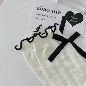 Detail of white knit socks featuring black ruffle trim and silk ribbon bow decoration