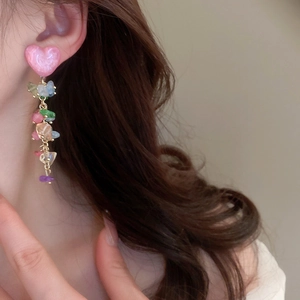 Détail de boucles d'oreilles cœur rose avec pampilles en gravier coloré sur modèle
