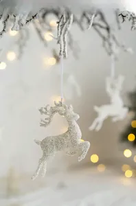 Close-up of sparkling white reindeer ornament with silver glitter on snow branch