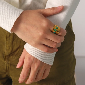 Detail of a gold wide textured ring with three green drop stones on a model hand