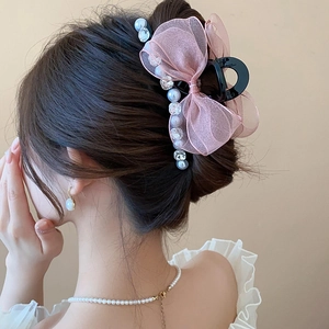 Detail of pink mesh bow hair claw with white pearls worn on blonde wavy hair