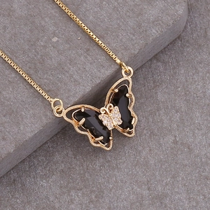 Macro shot of 18K gold butterfly necklace featuring black enamel wings and zircon center