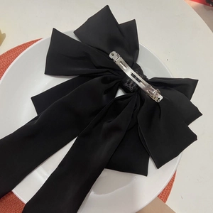 Large black satin ribbon bow hair clip on a white plate with elegant spring metal fastener