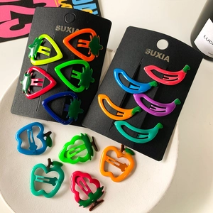 Detailed view of colorful fruit-shaped snap hair clips set on black card and in white bowl