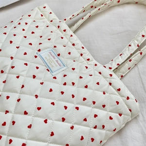 Close-up of white quilted tote bag featuring red heart patterns and logo fabric patch