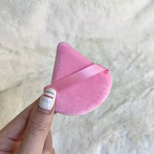 Close-up of a pink triangle powder puff with ribbon handle held against soft fabric