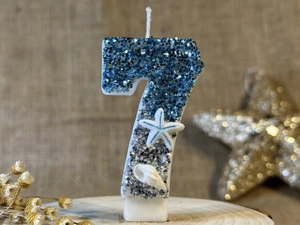 Detail of blue number 7 birthday candle with glitter starfish and shell decorations