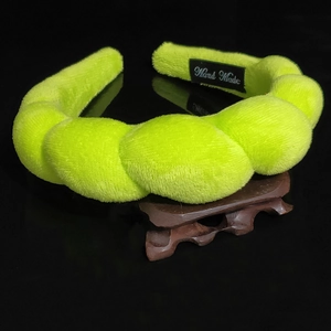 Macro detail of handmade braided neon green plush headband on a dark wooden display stand