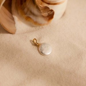 Macro shot of an iridescent pearl pendant with a gold clasp on a summer sandy beach