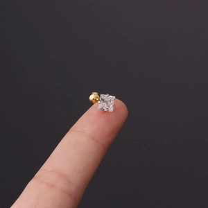 Macro shot of tiny gold ball back stud earring with a square zircon held on a fingertip