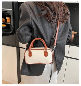 Detail of a color-block Boston bag featuring beige canvas and brown leather trim on a model