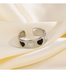 Macro detail of silver heart ring with black and white enamel on beige satin background