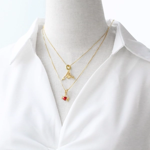 Golden dolphin and red heart wing pendant necklaces layered on model in white shirt