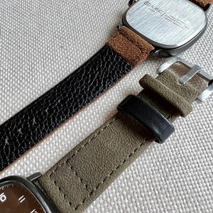 Detail of square watch case back and textured leather straps in black and olive green